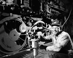 J.O. Haden, an African American engine supply man, poses with a smile in front of the wheels of a locomotive, holding a grease gun. “Lubritoriums” were locations at Norfolk & Western service facilities where workers could efficiently inspect and grease locomotives, using tools such as the Alemite grease gun. Haden, a longtime employee for N&W, was eventually promoted to the position of machinist. 