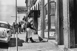 <p>A storekeeper sweeps the sidewalk in front of his storefront on 279 West Main Street, part of the commercial district that served Black Charlottesville residents.</p>